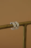 Silver hoop earrings on a gold stand against a brown background