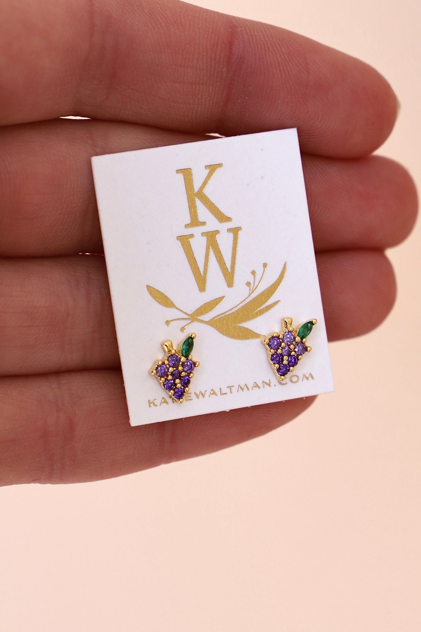 Gold and purple "grape" earrings on a white card with 'KW' branding held by a hand.