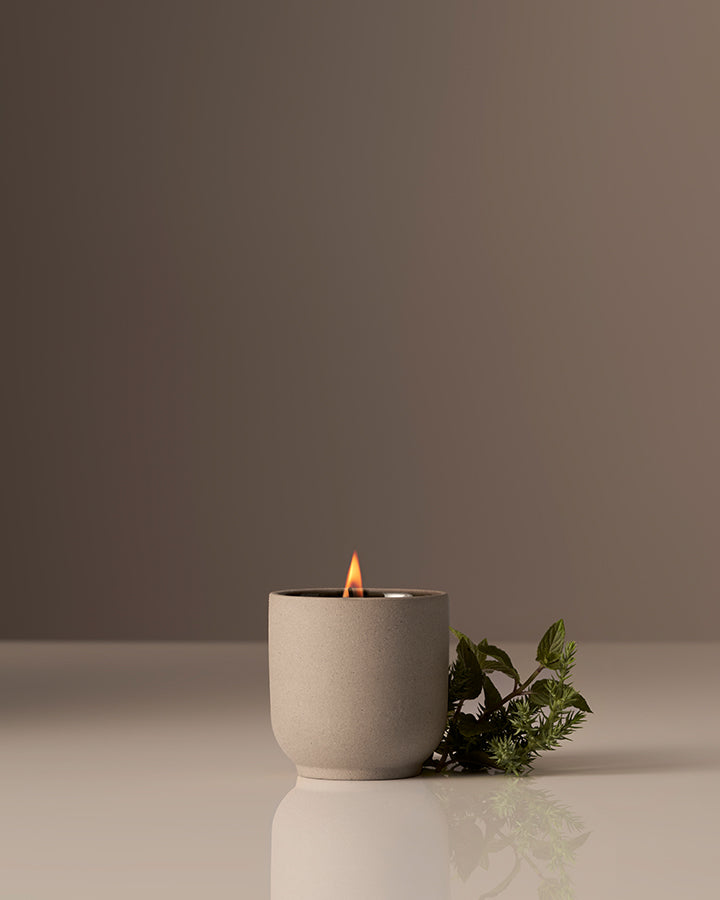 Ceramic candle holder with a lit candle on a reflective surface against a plain background