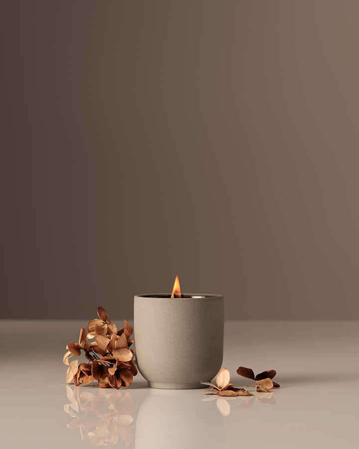 Candle in a gray pot with dried flowers on a reflective surface and dark background