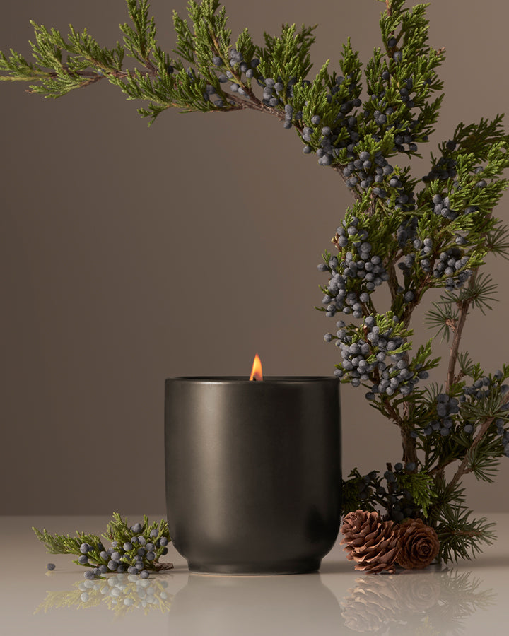 Black candle in a pot with greenery and berries on a neutral background
