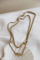 Gold chain necklace on a white shell with a neutral background