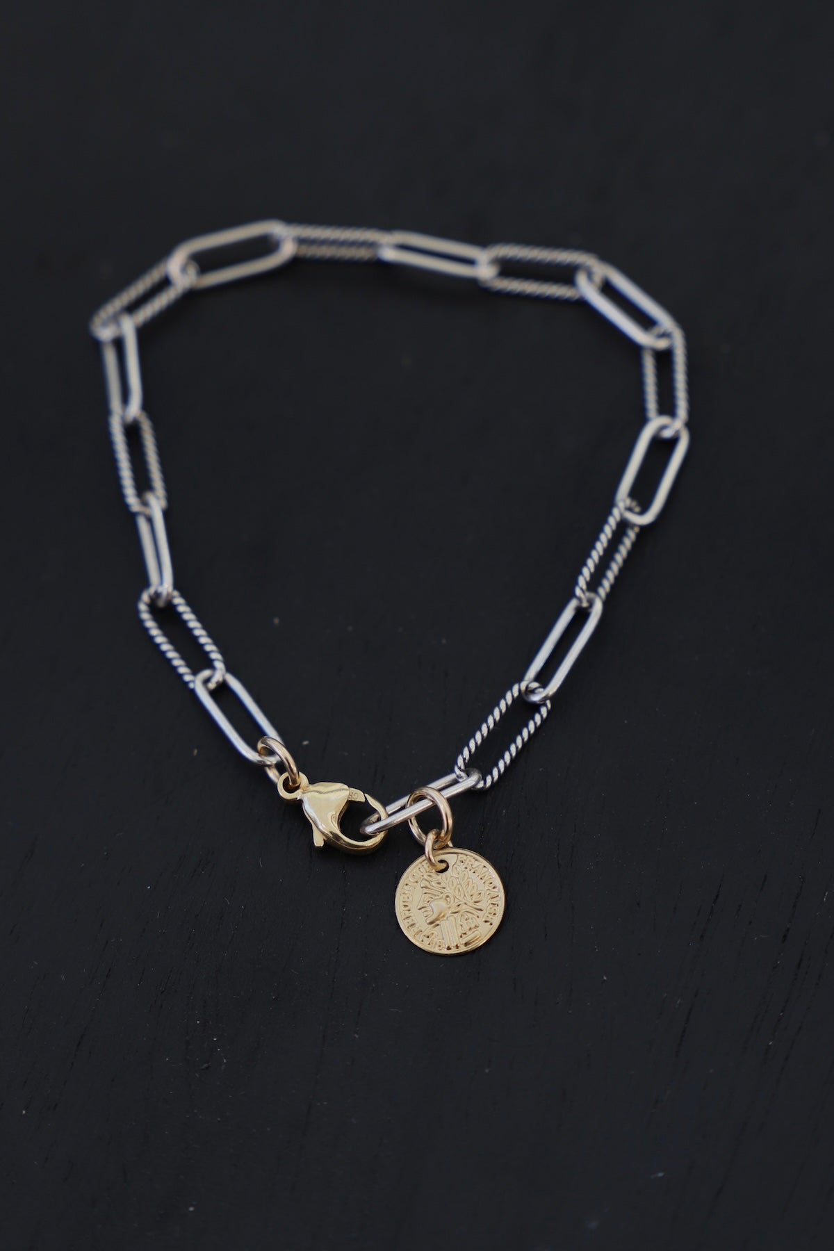 Silver chain bracelet with gold charms on a black background