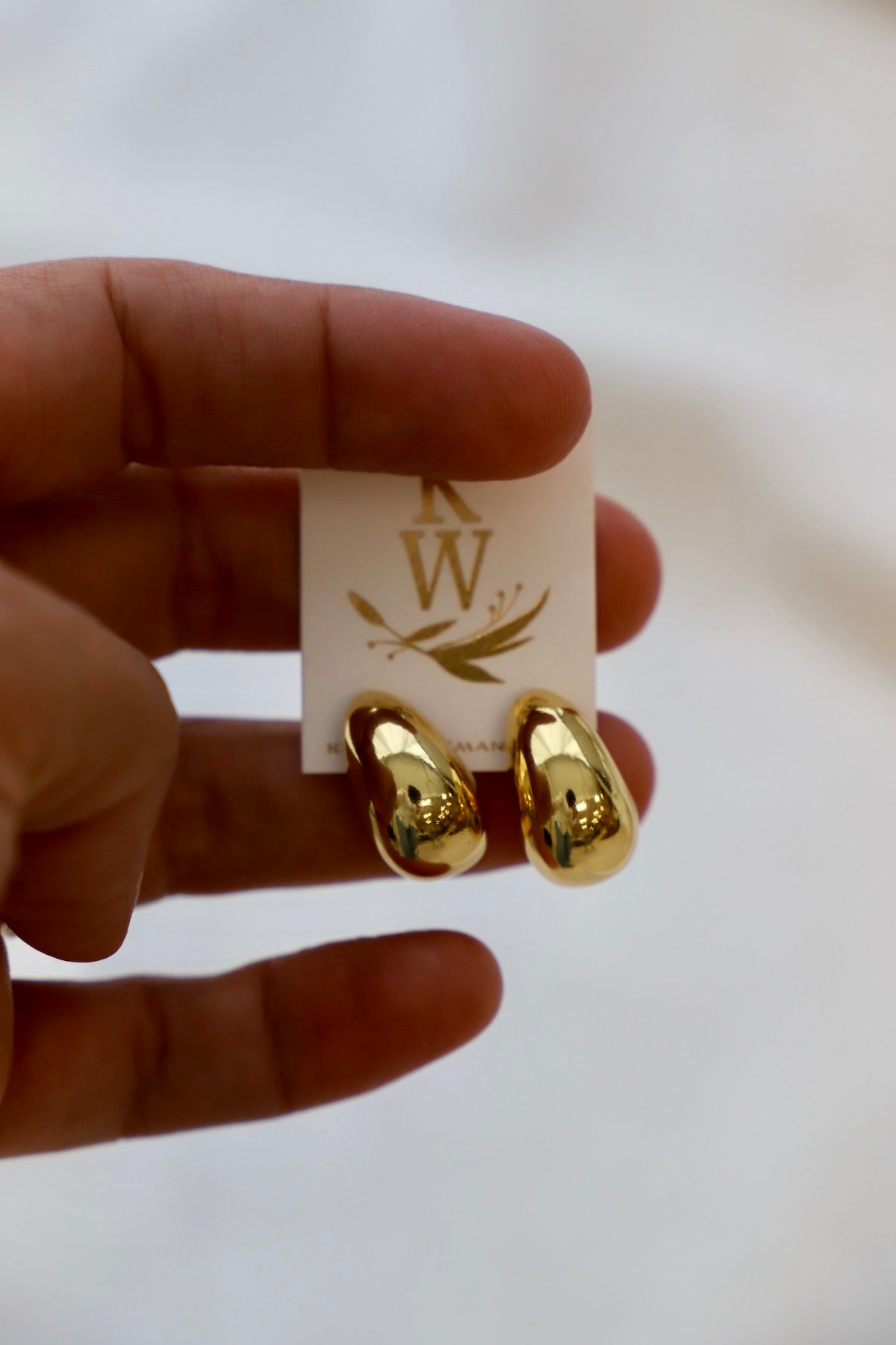 Gold chunky earrings held by a hand with a branded card in the background