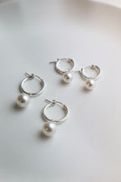 Set of silver hoop earrings with pearls on a light background