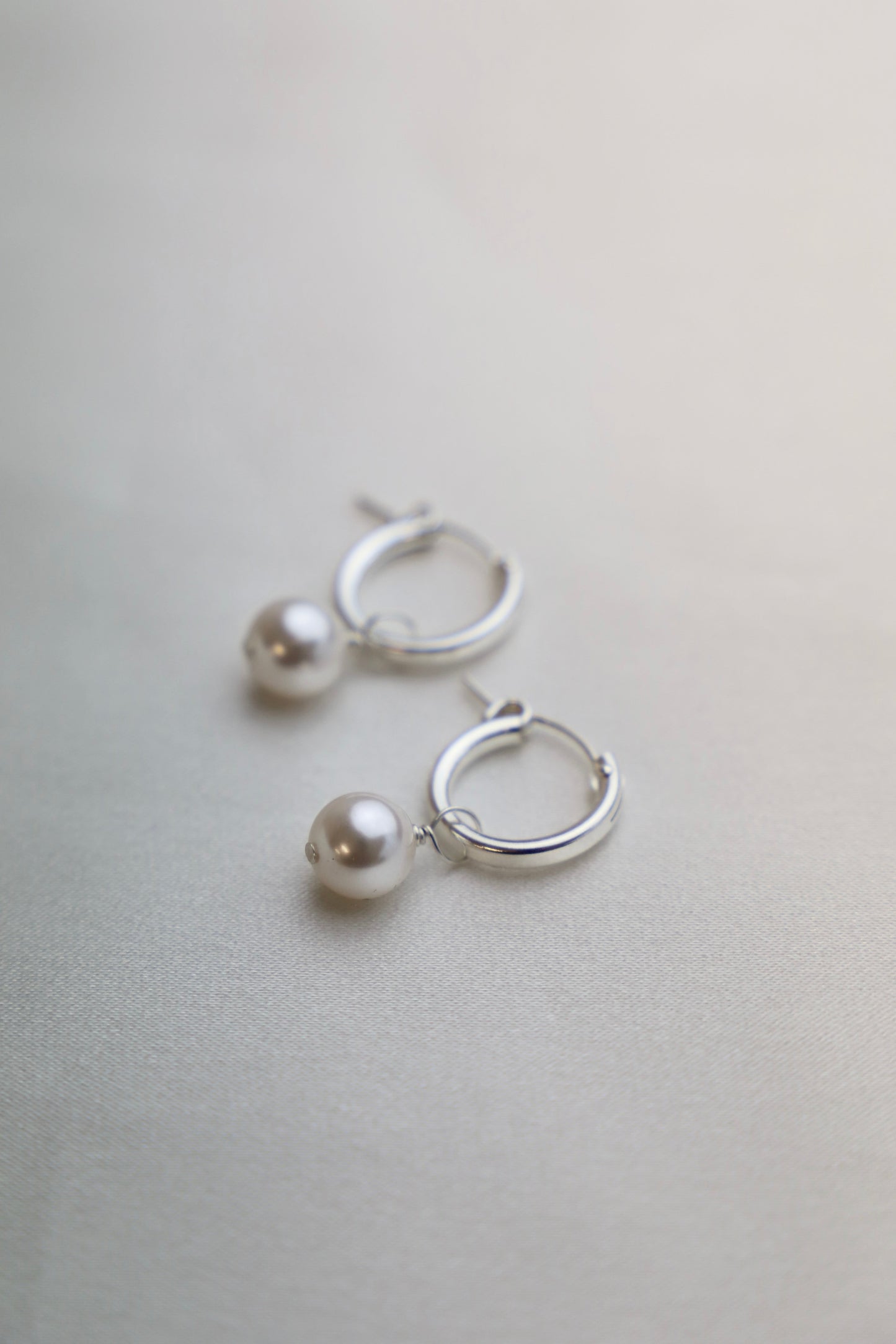 Silver hoop earrings with pearl accents on a light gray background