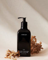 Black bottle of Homecourt laundry concentrate with dried flowers on a beige background