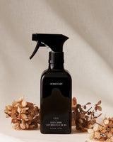 Black spray bottle labeled 'HOMEcourt' with dried flowers on a neutral background