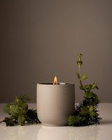 Candle in a gray ceramic holder with greenery on a neutral background