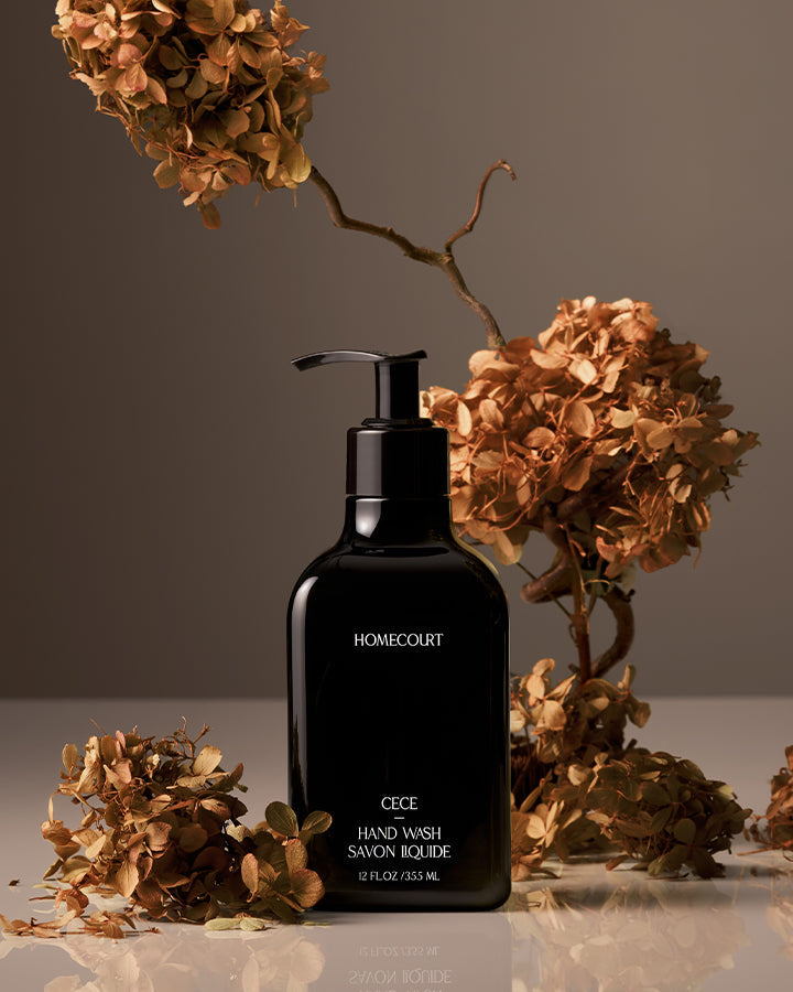 Black bottle of HOMECOURT CICÉ Handwash with dried flowers on a reflective surface.