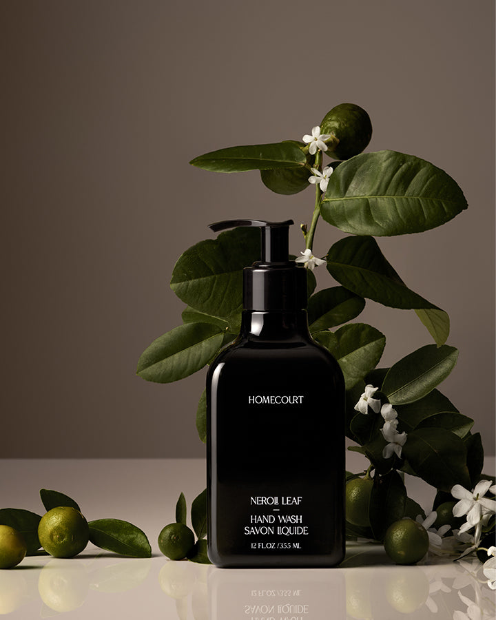 Black bottle of Homecourt Neroli Leaf Hand Wash with green leaves and limes in the background