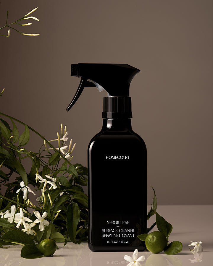 Black spray bottle labeled 'Homecourt' with green leaves and white flowers in the background