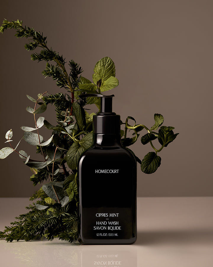 Black bottle of Homecourt Citrus Mint Hand Wash with green leaves on a neutral background