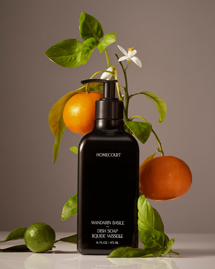 Black dish soap bottle labeled 'Homecourt' with mandarin oranges and basil leaves on a neutral background
