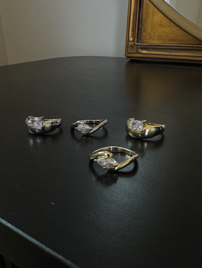 Four diamond rings on a dark surface with a mirror in the background