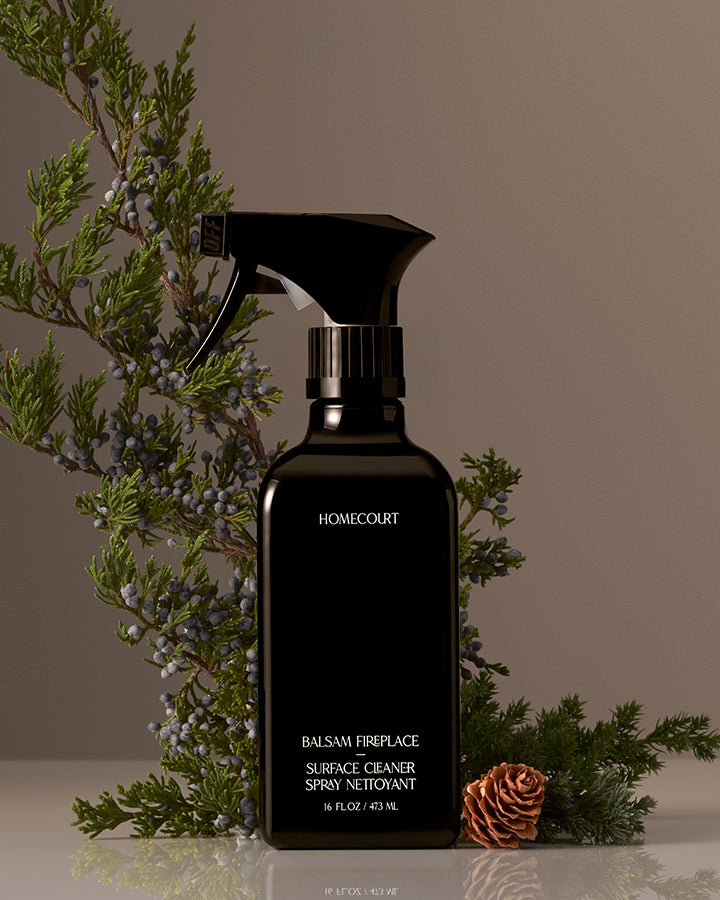 Black spray bottle labeled 'Homecourt' with decorative evergreen branches on a neutral background