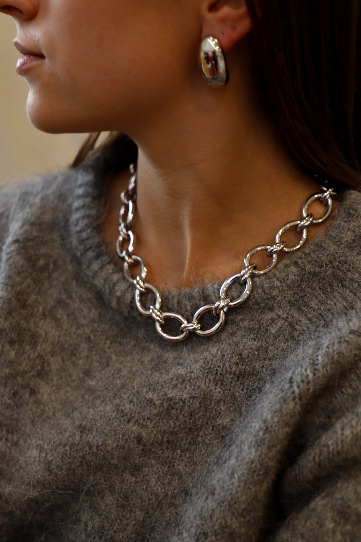 Close-up of a person wearing a silver chain necklace and gold hoop earrings.