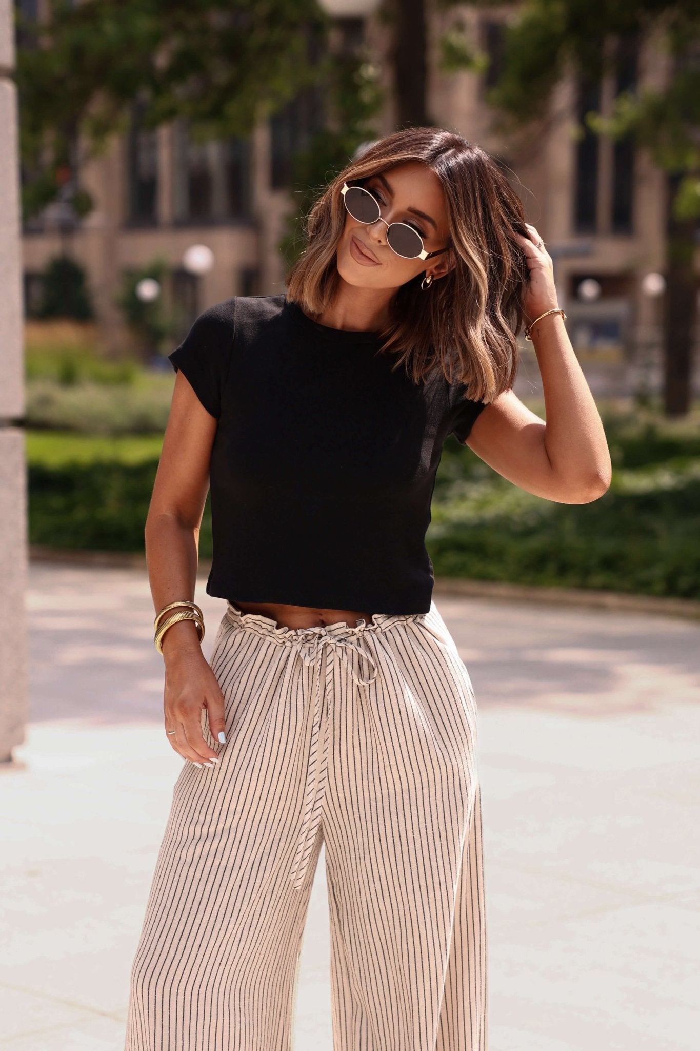 Woman wearing a black top and beige striped pants outdoors.