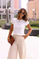 Woman wearing a white t-shirt and beige pants with sunglasses outdoors.