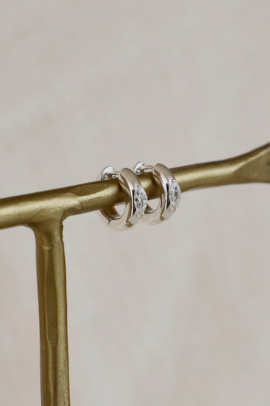 Silver hoop earrings with marquise cubic zirconia stone on a gold branch against a beige background
