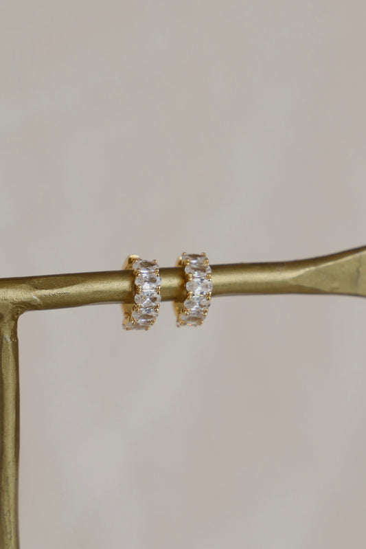 Gold hoop earrings on a gold stand against a neutral background
