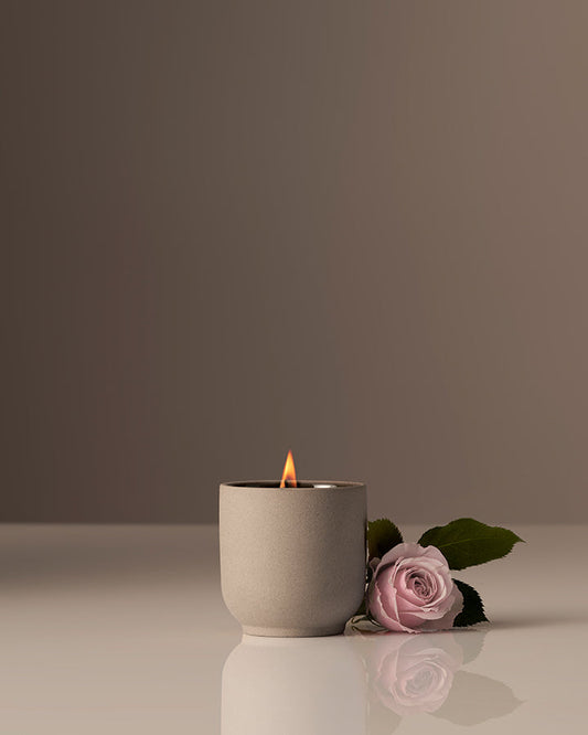 Candle in a gray holder with a pink rose on a reflective surface and dark background