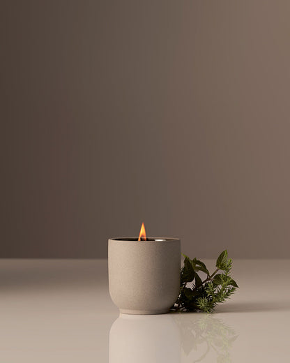 Ceramic candle holder with a lit candle on a reflective surface against a plain background