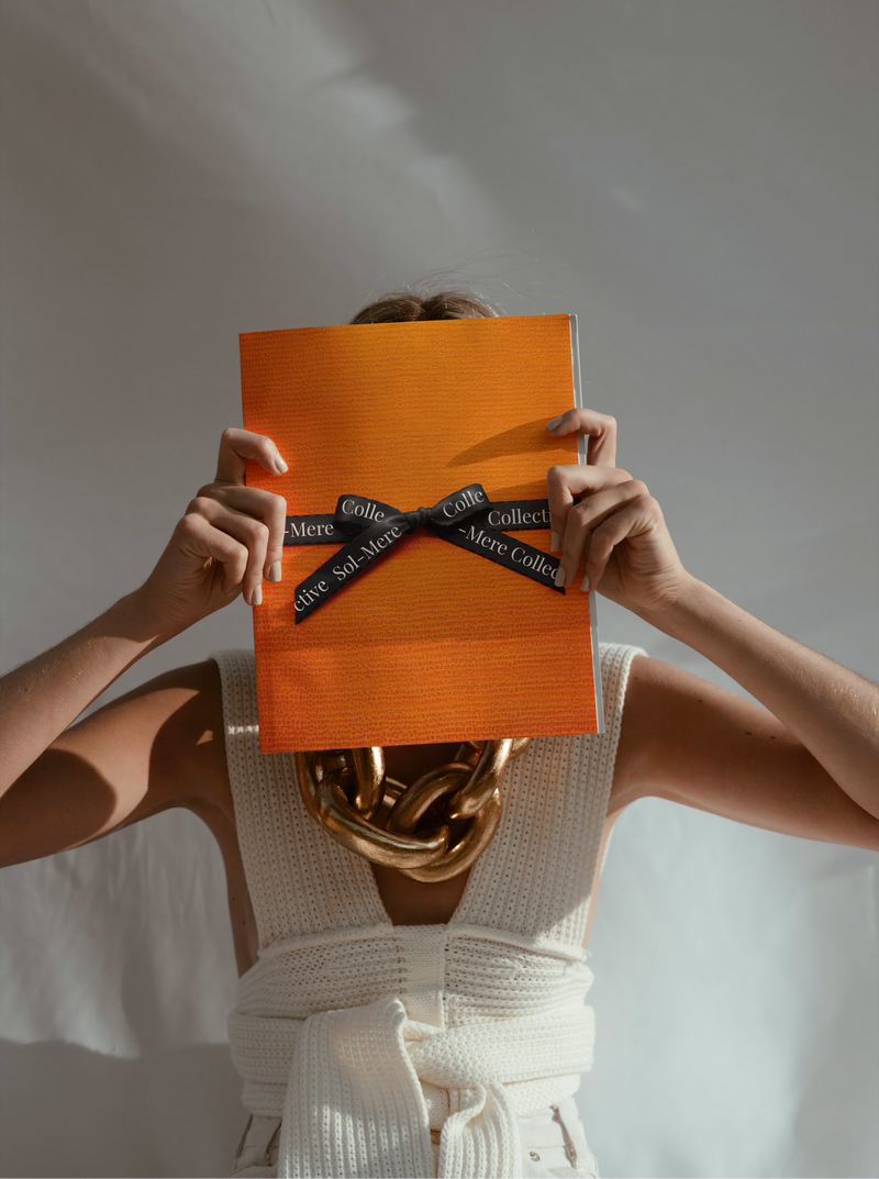 Person holding an orange book with a black ribbon marker against a white background