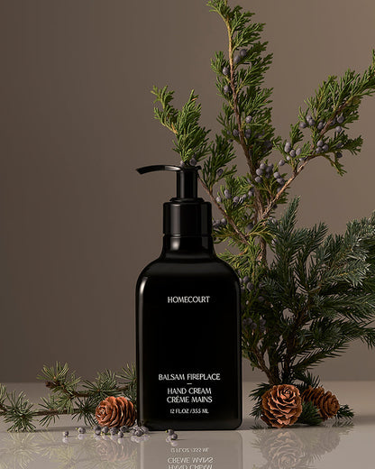 Black hand cream bottle labeled 'Homecourt' with greenery and pinecones on a neutral background