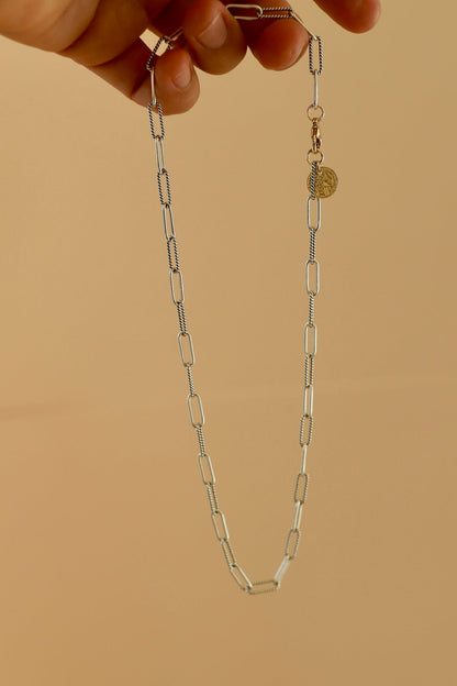 Gold chain necklace held by a hand against a beige background