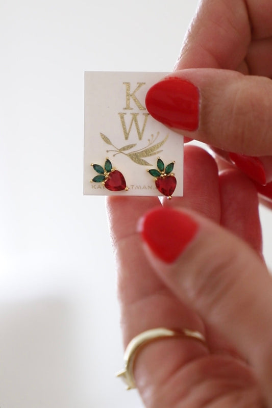 Hand holding a card with strawberry earrings and 'K W' branding.