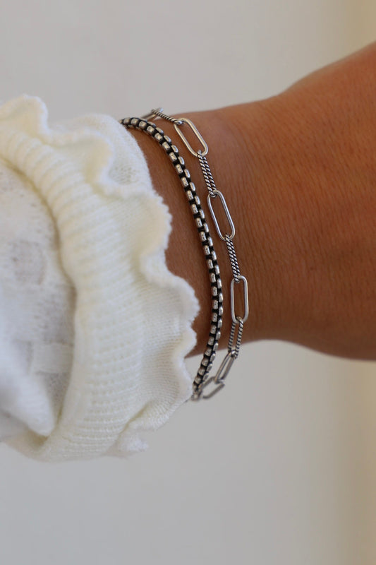 Close-up of a wrist wearing multiple silver chain bracelets on a blurred background