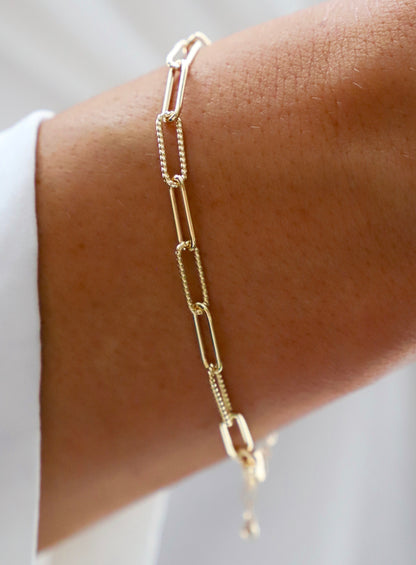 Gold chain bracelet on a wrist with a neutral background