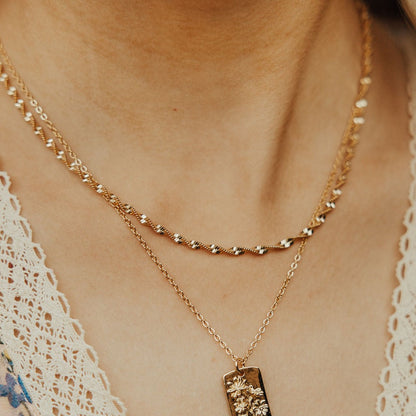 Gold necklace with a pendant on a person wearing a lace garment.