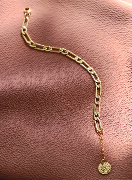 Gold chain bracelet with a pendant on a pink leather surface