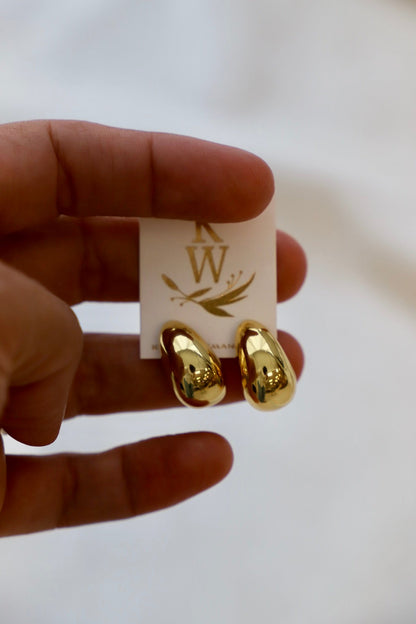 Gold chunky earrings held by a hand with a branded card in the background