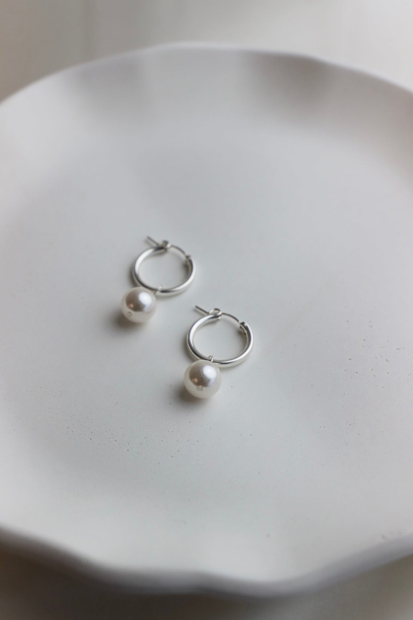 Silver hoop earrings with pearls on a white dish