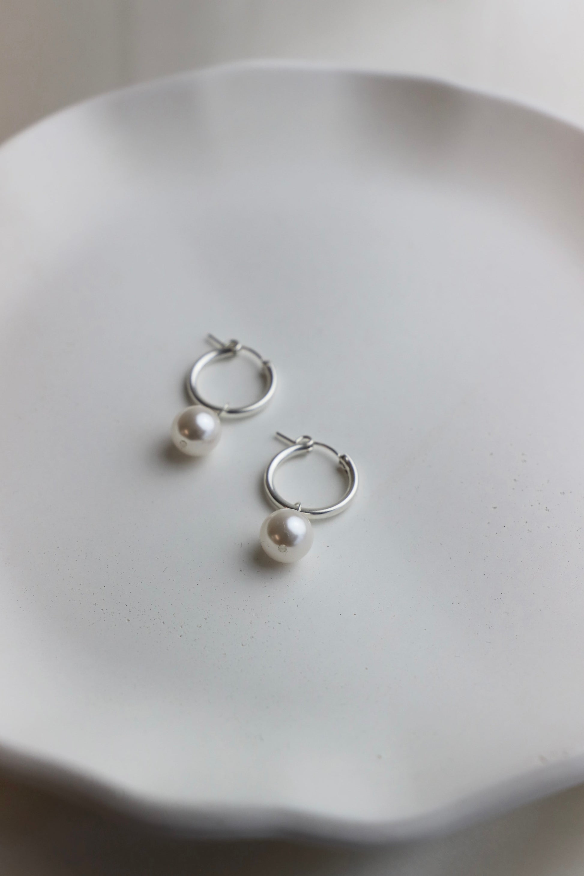 Silver hoop earrings with pearls on a white dish