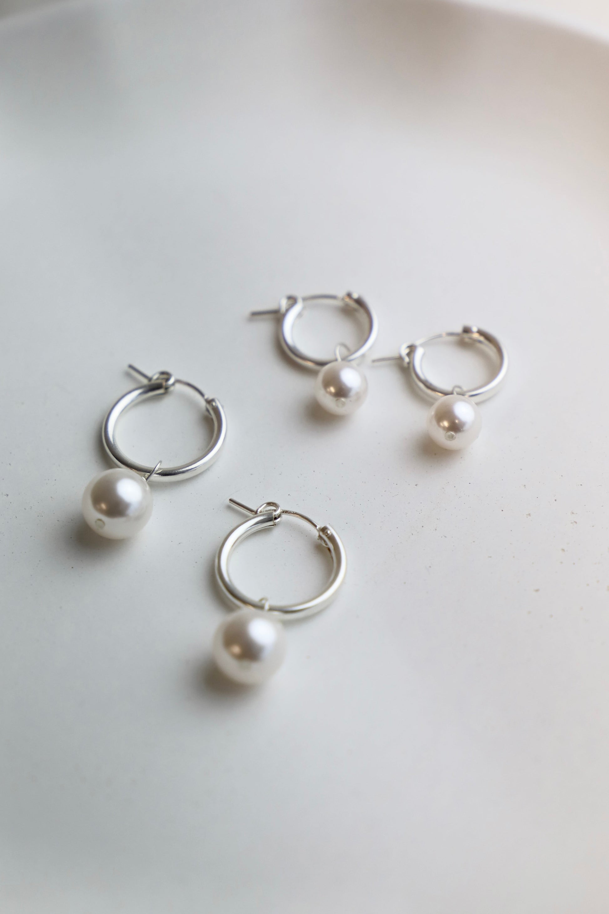 Set of silver hoop earrings with pearls on a light background