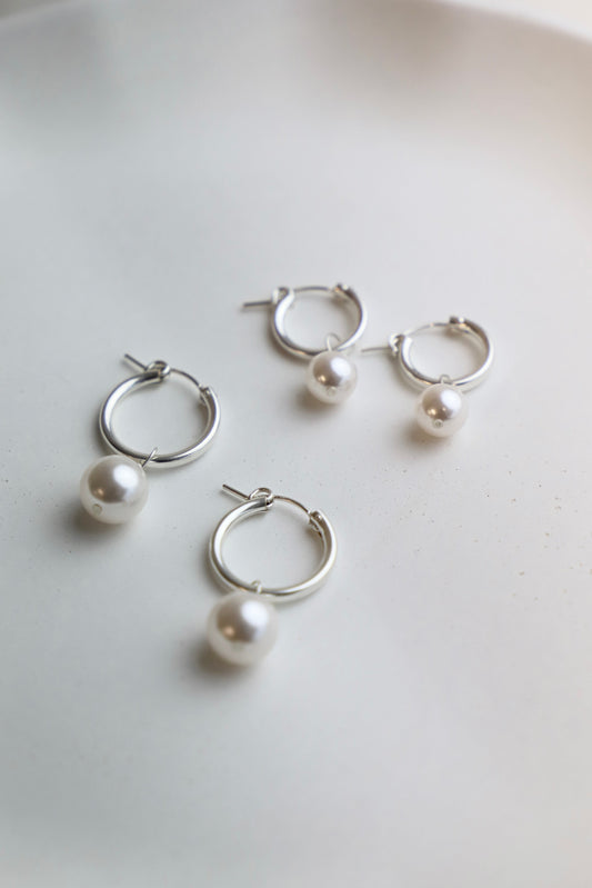 Set of silver hoop earrings with pearls on a light background