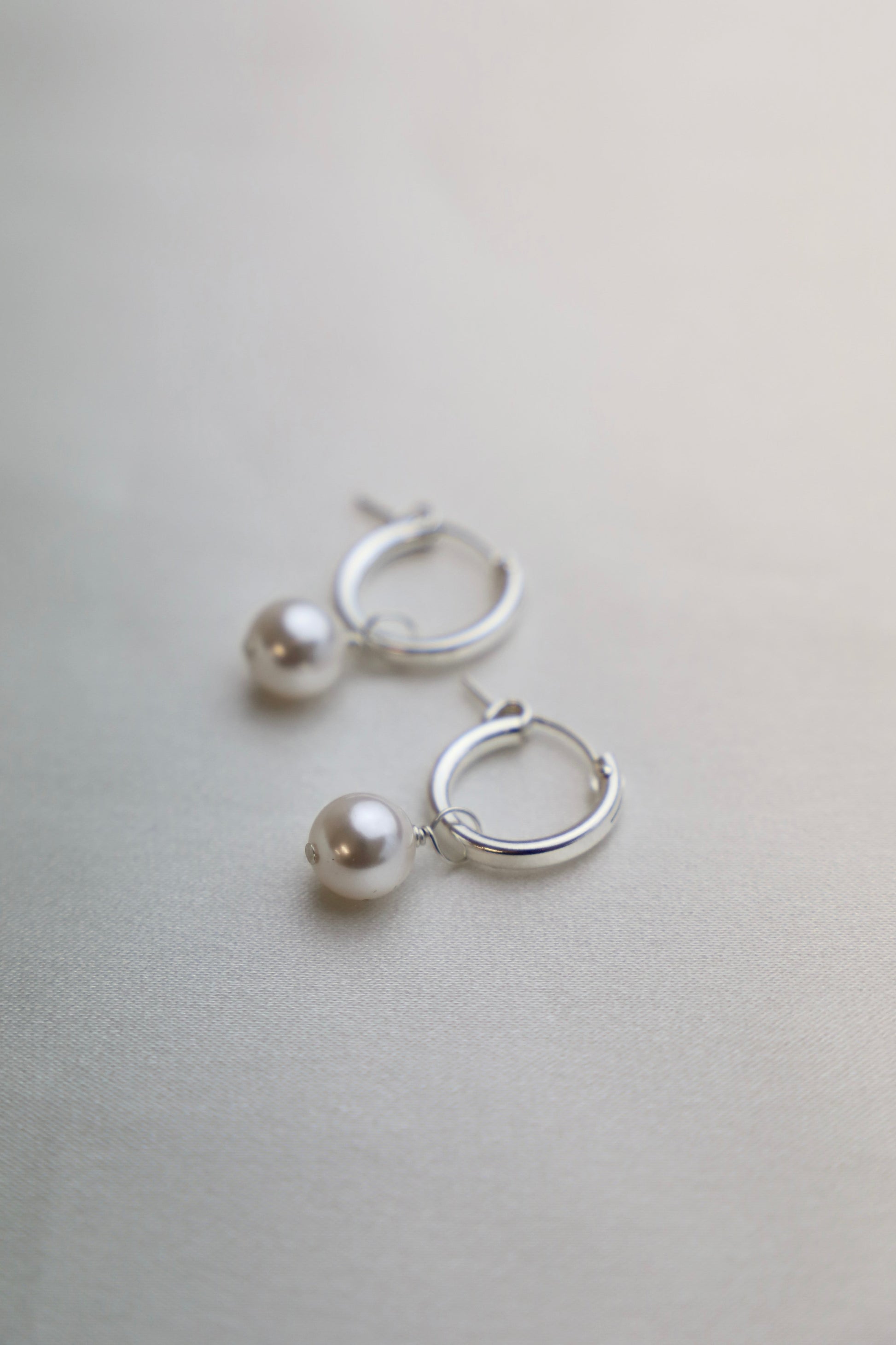 Silver hoop earrings with pearl accents on a light gray background