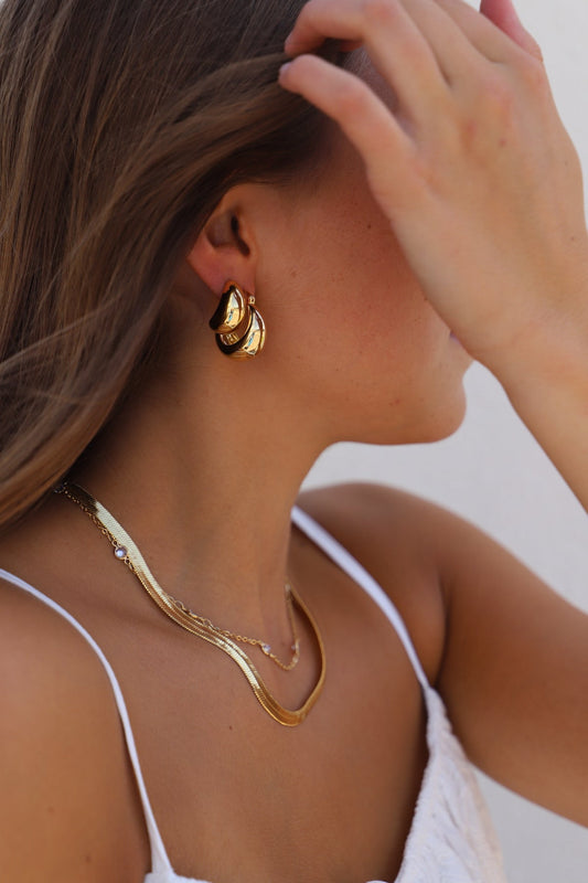 Close-up of a person wearing gold hoop earrings and necklace against a neutral background