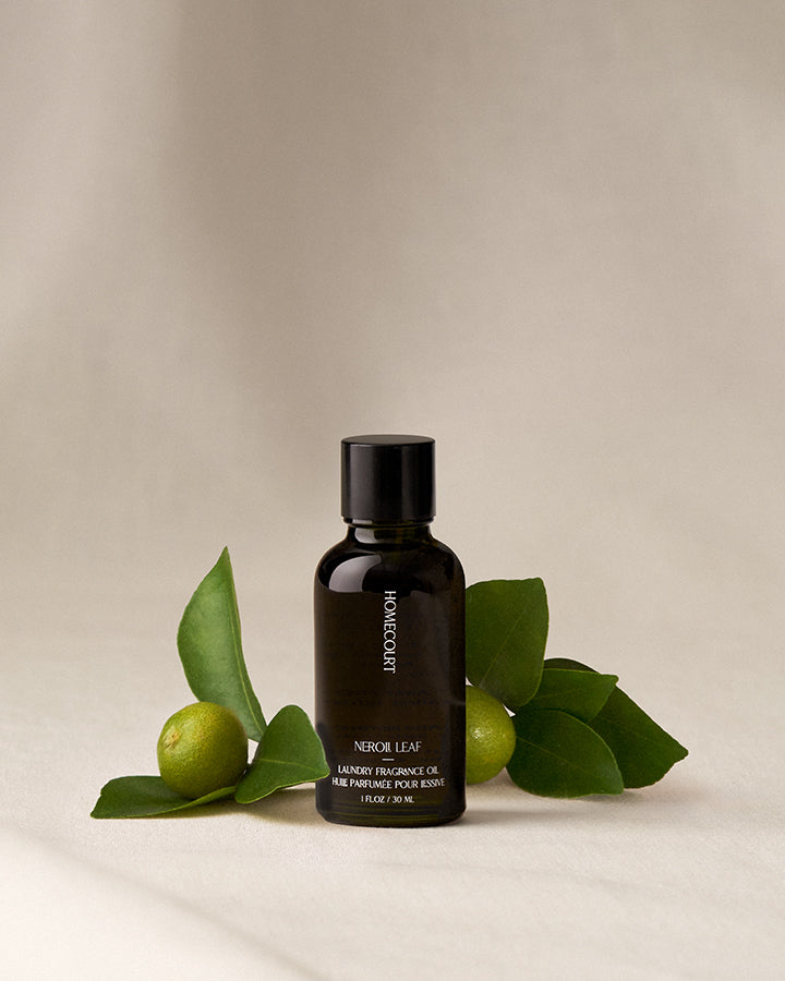 Black bottle of Homecourt Neroli Leaf fragrance oil with green leaves on a beige background
