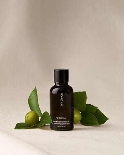 Black bottle of Homecourt Neroli Leaf fragrance oil with green leaves on a beige background