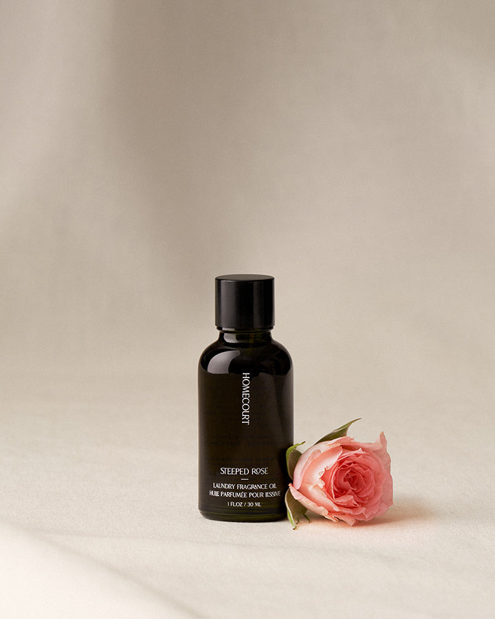 Black bottle of Homecourt Steeped Rose Lavender Fragrance Oil with a pink rose on a beige background