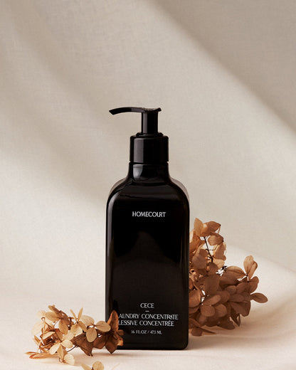Black bottle of Homecourt laundry concentrate with dried flowers on a beige background