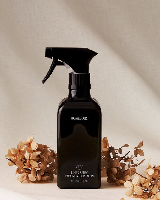 Black spray bottle labeled 'HOMEcourt' with dried flowers on a neutral background