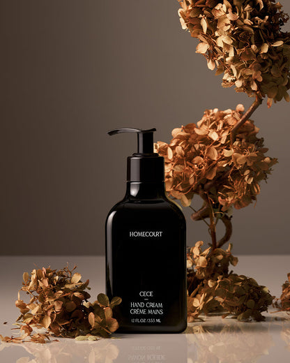 Black hand cream bottle labeled 'Homecourt' with dried flowers on a reflective surface.