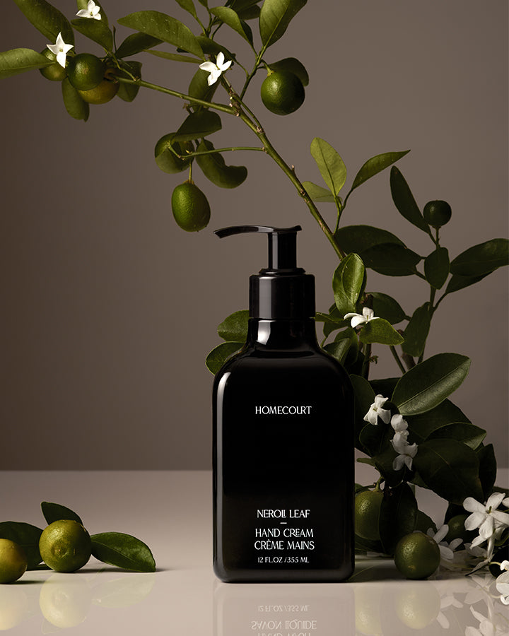 Black hand cream bottle labeled 'Homecourt' with green leaves and fruits in the background