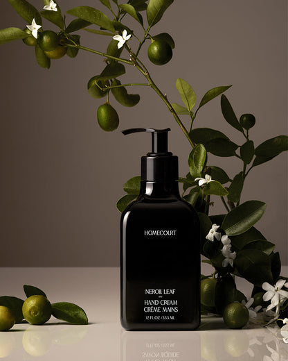 Black hand cream bottle labeled 'Homecourt' with green leaves and fruits in the background
